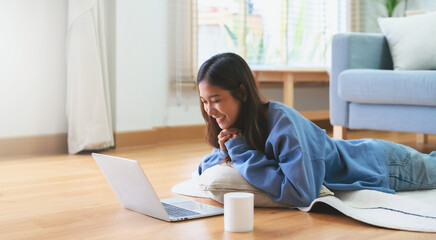 Young asian woman smile working in living room at home. Happy female using computer laptop and lying on the floor at house, Video call with friend