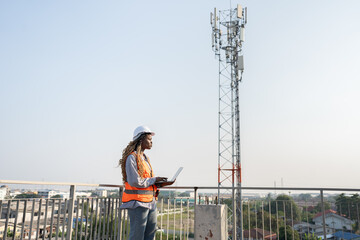 Portrait very tired worker African woman holding notebook computer and Signal antenna or Telecommunication Towers background with sky at construction site	 - 756174396