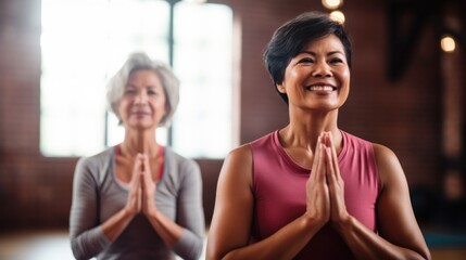 A middle-aged woman with short, elegant hair and a cheerful Asian woman practice yoga poses in the gym. - obrazy, fototapety, plakaty