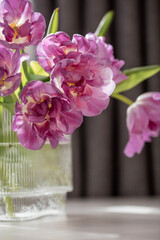 A bouquet of pink tulips in a beautiful stylish vase on the table in the room. The concept of the onset of spring and International Women's Day on March 8.