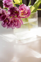 A bouquet of pink tulips in a beautiful stylish vase on the table in the room. The concept of the onset of spring and International Women's Day on March 8.