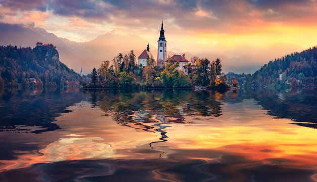 Pilgrimage Church of the Assumption of Maria and foggy mountains reflected in the calm waters of Bled lake. Calm autumn scene of Julian Alps. Great sunrise in Slovenia. Traveling concept background.