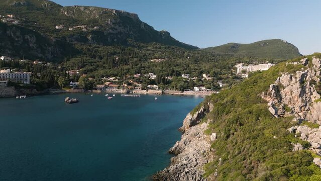 Drone orbit past sloping rock cliff to reveal Corfu Greece bay and beach