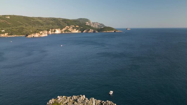 Aerial pullback showcases sharp textured rock cliffs and windswept waters of Corfu Greece