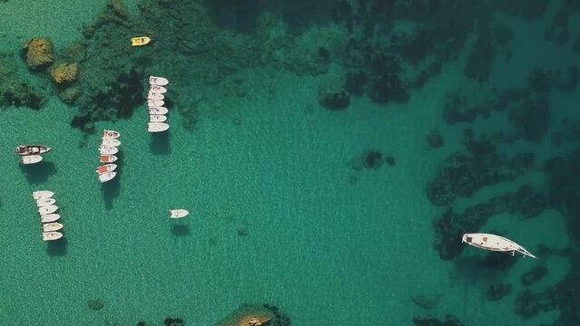 Top down aerial overview pans across small skiff and sailboats anchored below rocky cliffs of Corfu Greece
