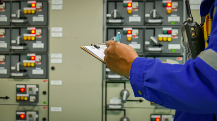 A man is writing on a clipboard in front of a row of electrical panels