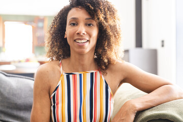 Biracial woman with curly brown hair smiles warmly, wearing a colorful striped top - Powered by Adobe