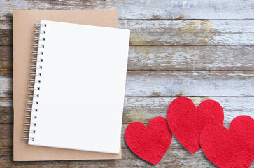 Red paper heart and notebook on wooden table background.