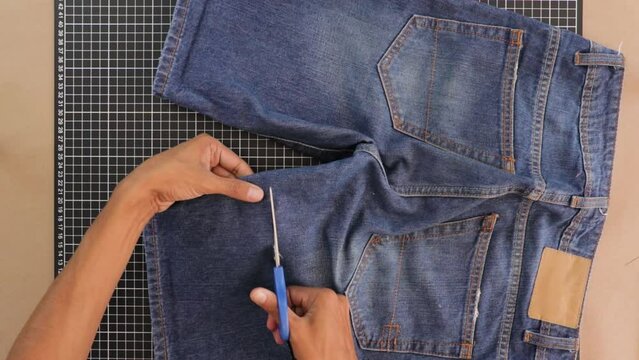 Person remodeling and cutting short trousers with scissors. Close up