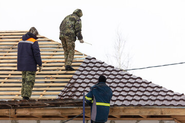 Workers install tiles on the roof of a house in winter