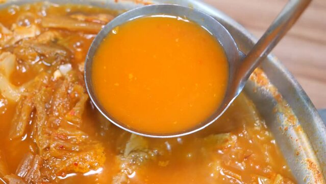 보글보글 끓은 묵은지 갈비전골의 감칠맛 나는 빨간 국물을 국자로 뜨는 모습