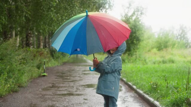 Happy child opens umbrella in rainy park