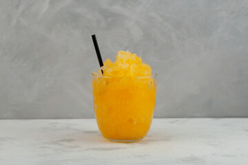 Overflowing glass of orange slush drink with drinking straw. Refreshing Slushie drink. Sweet Citrus...