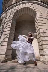 Stylish woman building city. A dancer in a long white skirt dances in front of a building with an...