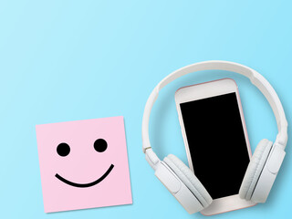 White headphone, smartphone and smiley symbol in pink sticky note on blue background.