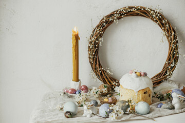 Stylish easter eggs, panettone, bunnies, cherry blossom and daffodils composition on rustic table....