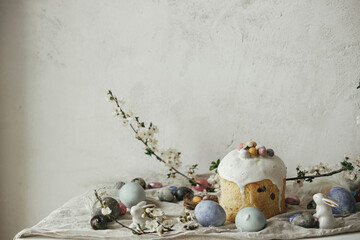 Stylish easter eggs, panettone, bunnies, cherry blossom composition on rustic table. Happy Easter!...