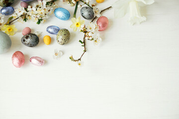 Easter flat lay. Stylish easter eggs and cherry blossom on white rustic table. Happy Easter, space for text. Modern natural dyed and chocolate eggs and spring flowers. Easter minimal banner