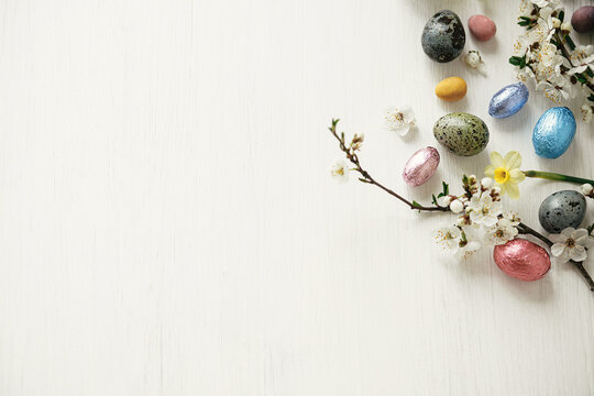 Easter flat lay. Stylish easter eggs and cherry blossom on white rustic table. Happy Easter, space for text. Modern natural dyed and chocolate eggs and spring flowers. Easter minimal banner