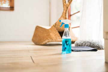 Spray bottle in a side view with blue liquid detergent inside on the wooden floor with rag and grey...