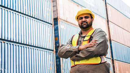 An attractive Indian male industrial engineer in yellow hard hat, safety vest with a blurred container yard in background. Working in the logistics center. Inspector, supervisor in container terminal. - 756226308