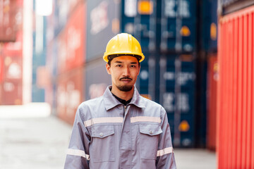 Attractive Japanese man industrial engineer in yellow hard hat, safety vest with a blurred container yard in background. Working in the logistics center. Inspector, supervisor in container terminal. - 756226582