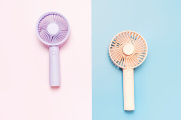 Small portable mini fans on blue and pink background close-up.