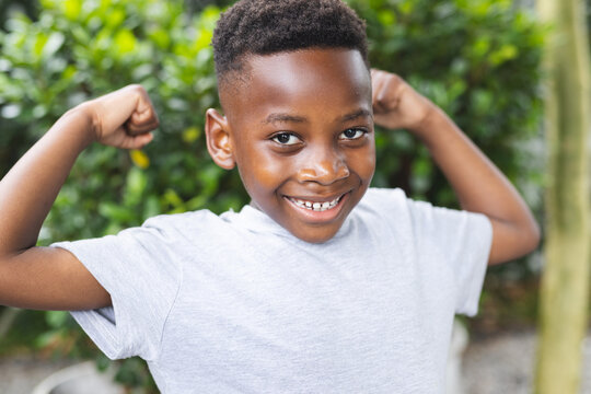 African American boy flexes his muscles with a confident smile in a garden