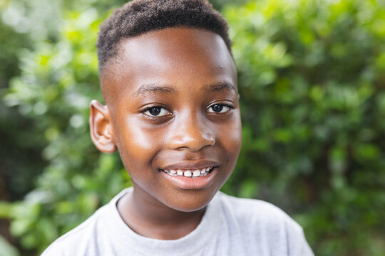 African American boy smiles brightly, surrounded by lush greenery in a garden