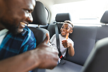 African American father and son share a joyful moment in a car, both giving thumbs up