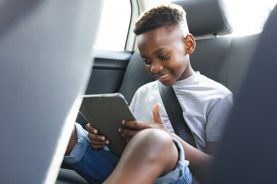 African American boy enjoys a tablet in the backseat of a car - Powered by Adobe