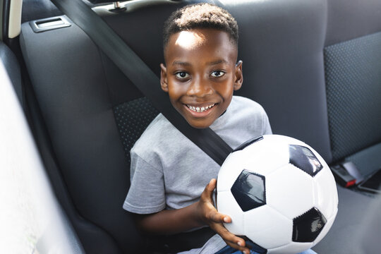 African American boy smiles while holding a soccer ball in a car - Powered by Adobe