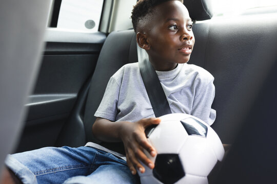 African American boy sits in a car holding a soccer ball, wearing a seatbelt - Powered by Adobe