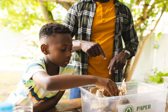 African American boy sorts paper for recycling under the guidance of his father