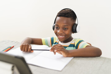 African American boy with headphones studies online at a desk