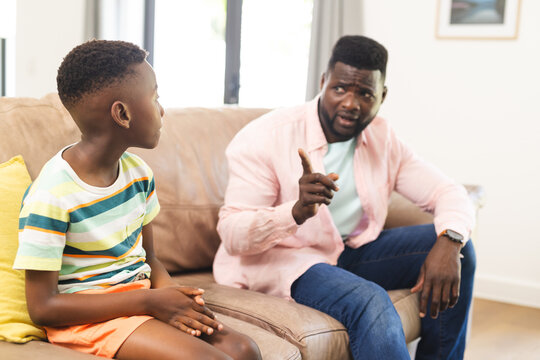 African American father in a pink shirt appears to be giving advice to a young son