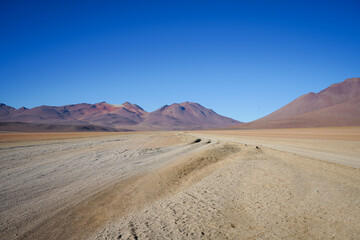 Fototapeta na wymiar Dirt Tracks in Red Sand Desert, Blue Sky Background - Salar de Uyuni, Bolivia 