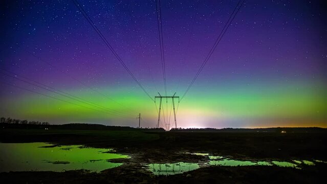 Time-lapse of a aurora polaris and clouds moving over electric wires on a wet field