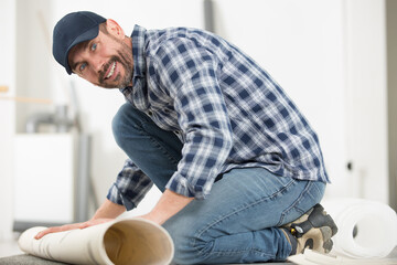 male handyman rolling carpet on floor at home