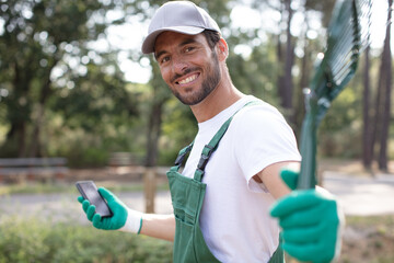 male gardener holds a rake and a smartphone