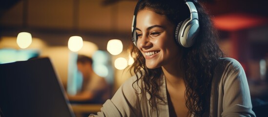 A happy woman wearing headphones is smiling while using a laptop computer to enjoy entertainment...