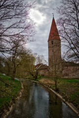 Der Eckturm einer mittelalterlichen Stadtmauer an einer Flussbiegung mit Bäumen aum Ufer und...