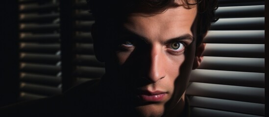 A closeup shot capturing the mans jaw and eyelashes behind blinds, in darkness. The flash photography highlights the art of his facial features. He looks pleased, possibly at a special event