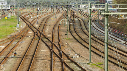 A network of brown rusted railroad tracks and overhead lines at a railroad station
