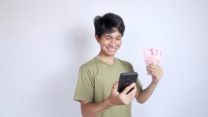 smiling asian man looking at mobile phone and holding money