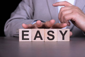 EASY, the word is written on wooden cubes, blocks on the background of a man, a businessman in a...
