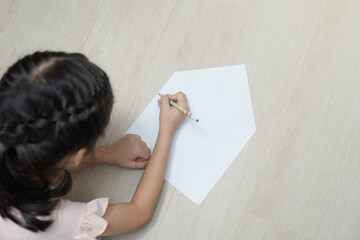 A girl is drawing something on white paper in the shape of a simple house.