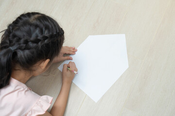 A girl is drawing something on white paper in the shape of a simple house.