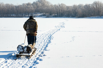 A lonely old hermit, in winter, crosses the river on ice and pulls a sled with firewood for heating