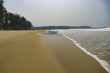 People enjoying at beautiful brown sand beach. Forest and hill at beach. Sea waves foaming around...